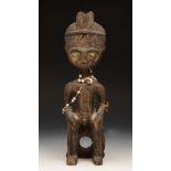 AN AFRICAN TRIBAL CARVED WOODEN FIGURE of a seated man with feathered headband and bead ornament