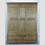 A pine triple wardrobe, with an arrangement of five drawers below,