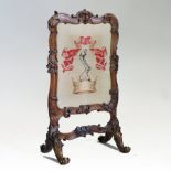 A Victorian carved walnut firescreen, inset with a woolwork family crest,