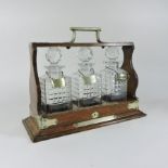 An early 20th century brass mounted oak tantalus, containing three cut glass decanters and stoppers,
