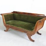 An early 19th century carved mahogany and green upholstered scroll end sofa, on sabre legs,