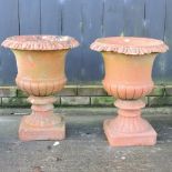 A pair of red terracotta campana shaped garden urns, each on a pedestal base,