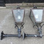 A large pair of exterior metal wall lanterns, each on a black painted cast iron support,