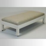 A large carved wooden and white painted foot stool, upholstered in gold, on square legs and castors,