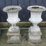 A pair of reconstituted stone campana shaped urns, with relief decoration, on pedestal bases,