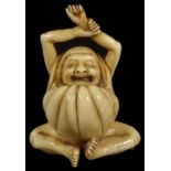 ˜A JAPANESE IVORY NETSUKE OF DARUMA, MEIJI PERIOD, CIRCA 1900 seated, stretching and yawning, signed