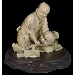 ˜A JAPANESE IVORY OKIMONO OF A CRAFTSMAN, MEIJI PERIOD (1868-1912) carved kneeling and surrounded by