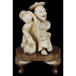 ˜A JAPANESE IVORY OKIMONO OF A MUSICIAN, MEIJI PERIOD (1868-1912) carved kneeling and holding a drum