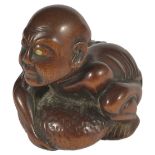 ˜A JAPANESE WOOD NETSUKE OF A BLIND MASSEUR, EARLY MEIJI PERIOD, CIRCA 1870 crouching to lift a