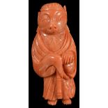 A JAPANESE CORAL NETSUKE OF A TRANSFORMING BADGER, MEIJI PERIOD (1868-1912) standing in a priest's