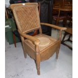 An Edwardian commode armchair with cane seat and back, original pot