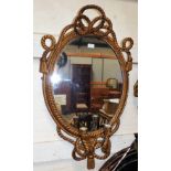 A wall mirror in gilt oval rope twist frame with bow pediment and scrolled twin sconces below