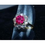 A yellow metal dress ring with a ruby and 8 diamonds in cluster setting, marks worn, test as 18