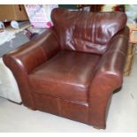 A brown leather armchair with loose cushions