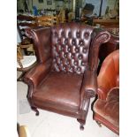 A brown leather deeply buttoned wing back armchair