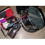 An Olympus lens M.Zuiko; a selection of other camera equipment; a chromed pearl snare drum in