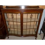 A 1930's oak serpentine front display cabinet enclosed by 2 doors