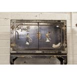 A CHINOISERIE DECORATED BLACK LACQUERED TWO-DOOR SIDE CUPBOARD, overlaid with figures on a