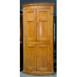 A VICTORIAN STAINED PINE BOW FRONTED CORNER CUPBOARD WITH PANELLED DOORS, 212CM H