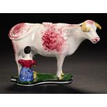 A WHITE EARTHENWARE COW CREAMER, 19TH C the cow sponged in pinkish red and standing beside a