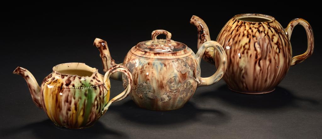 THREE TORTOISESHELL GLAZED CREAMWARE TEAPOTS AND A COVER ONE STAFFORDSHIRE, THE OTHERS POSSIBLY