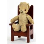 A WELL LOVED EARLY 20TH CENTURY TEDDY BEAR SEATED UPON A MINIATURE ARMCHAIR