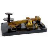 A BRASS MORSE KEY WITH EBONITE KNOB AND BASE, 18CM L, EARLY 20TH C