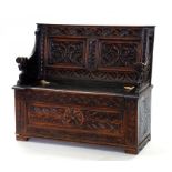 AN OAK BOX SETTLE PROFUSELY CARVED WITH FOLIAGE AND GROTESQUES, 103CM W, CIRCA 1900