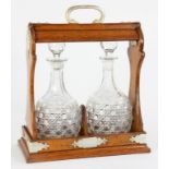 AN EPNS MOUNTED OAK TANTALUS, WITH A PAIR OF CUT GLASS DECANTERS AND STOPPERS, 38CM H, EARLY 20TH