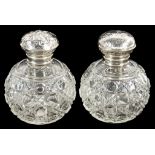 A PAIR OF CUT GLASS SPHERICAL SCENT BOTTLES, WITH ORNATE EMBOSSED SILVER SCREW-CAP, 11CM H,