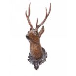 A CARVED AND STAINED WOOD WALL HANGING DEER'S HEAD TROPHY with antlers and ebonised oak leaf and