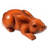 A JAPANESE CARVED AND STAINED WOOD NETSUKE IN THE FORM OF A CROUCHING HARE, 5CM L, SIGNED