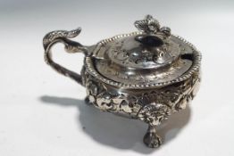 A Victorian silver cauldron shaped mustard pot embossed in high relief with flowers and leaf