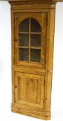 A pine standing corner cabinet, the upper section with arched glazed panel enclosing shelves,