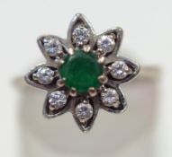 A diamond and emerald flower head cluster ring, the white mount stamped '18ct',