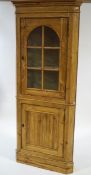 A pine standing corner cabinet, the upper section with arched glazed panel enclosing shelves,