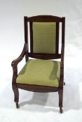 An Edwardian mahogany armchair with green patterned upholstery and scroll legs upon castors