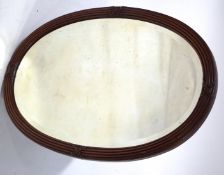 An oval mirror with reeded mahogany frame with crossed ribbon decoration,