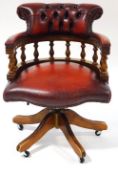 A leather and mahogany Captain's chair with button back on splayed legs with casters