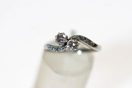 A two stone diamond cross over ring, the white mount stamped '18ct',