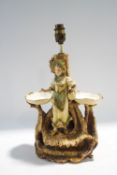 An Austrian ceramic figural table lamp, modelled as a lady in fine clothes upon a naturalistic base,