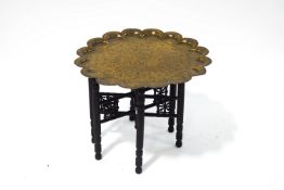 An Indian engraved brass tray on a carved wooden folding base,