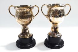 A matched pair of hammered silver two handled trophy cups, by Goldsmiths and Silversmiths Co Ltd,