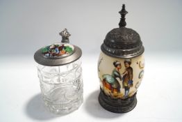 Two decorative German beer tankards, a press moulded glass one with porcelain inset lid,