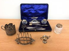 A cased silver manicure set; a miniature silver two handled trophy cup; a small silver toast rack;