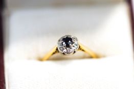 An 18 carat gold sapphire and diamond cluster ring, the round cut stone enclosed by single cuts,