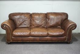 A leather four seater sofa with brass studding to arms and apron, upon turned wooden feet,