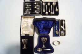 A silver egg cup with spoon; another silver egg cup with a spoon; a silver napkin ring;