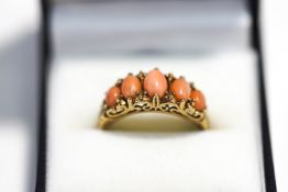 A 9 carat gold coral ring, the graduate cabochons to a Victorian style carved head mount,