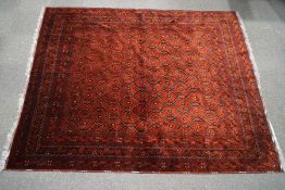 A Persian style carpet with central repeating medallion motif on a red field,